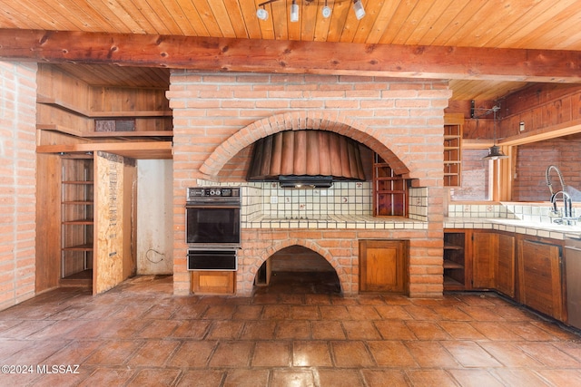 kitchen featuring beam ceiling, tile counters, wooden ceiling, backsplash, and oven