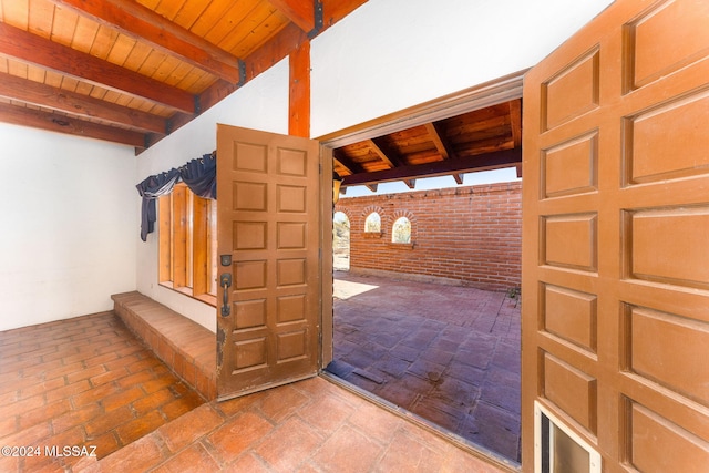 interior space with beamed ceiling, wooden ceiling, and brick wall