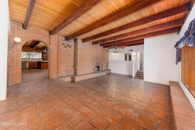 unfurnished living room with ceiling fan, beam ceiling, wood ceiling, and brick wall