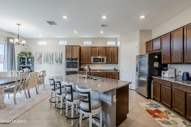 kitchen featuring light stone countertops, stainless steel appliances, hanging light fixtures, and an island with sink