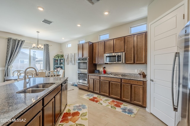 kitchen featuring stone counters, hanging light fixtures, sink, appliances with stainless steel finishes, and a notable chandelier