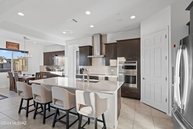 kitchen featuring sink, wall chimney range hood, a kitchen island with sink, dark brown cabinets, and appliances with stainless steel finishes