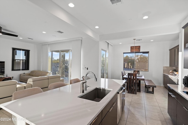 kitchen featuring dishwasher, a kitchen island with sink, sink, light tile patterned floors, and dark brown cabinetry