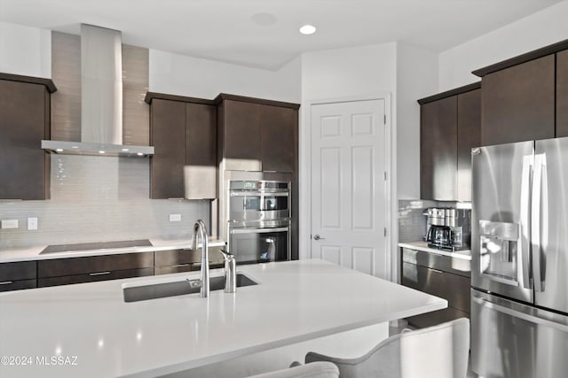 kitchen featuring a kitchen breakfast bar, sink, wall chimney exhaust hood, appliances with stainless steel finishes, and tasteful backsplash