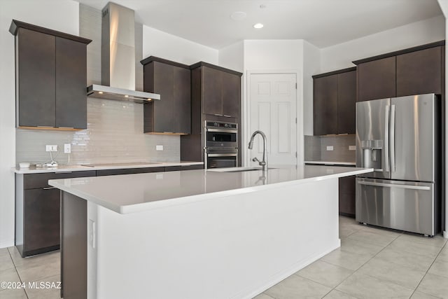 kitchen with sink, wall chimney range hood, an island with sink, and appliances with stainless steel finishes