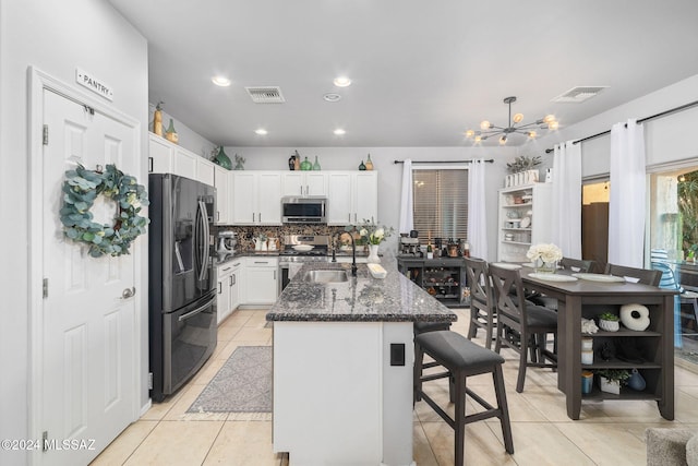 kitchen with appliances with stainless steel finishes, white cabinetry, a kitchen breakfast bar, dark stone counters, and a center island with sink