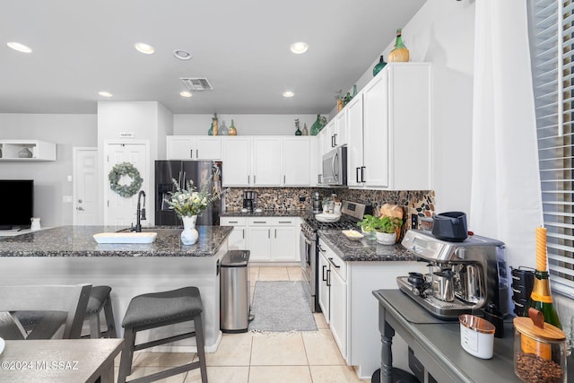 kitchen featuring sink, white cabinetry, stainless steel appliances, decorative backsplash, and dark stone counters