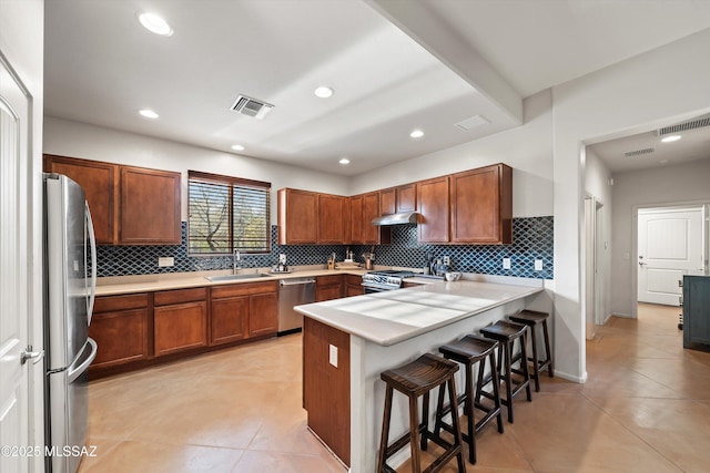 kitchen with kitchen peninsula, appliances with stainless steel finishes, a kitchen breakfast bar, sink, and light tile patterned floors