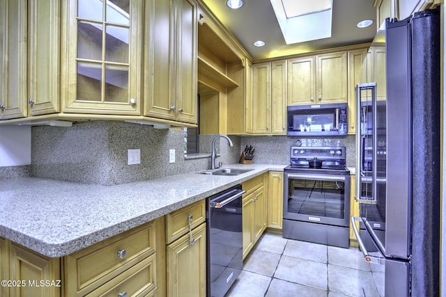 kitchen featuring appliances with stainless steel finishes, a skylight, sink, light tile patterned floors, and light stone countertops