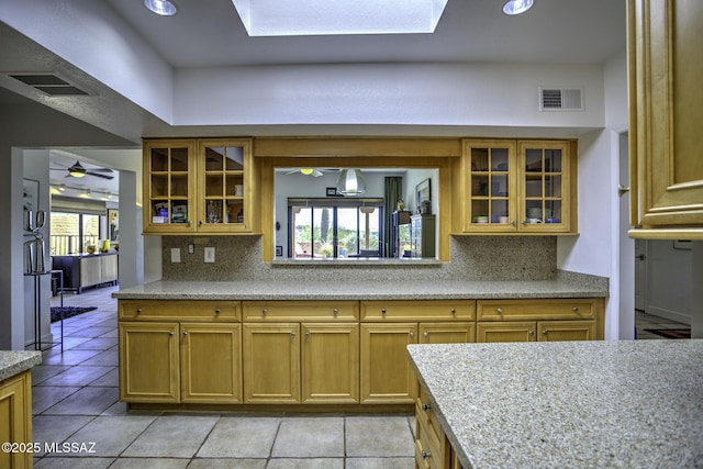 kitchen with backsplash, light tile patterned floors, light stone countertops, and ceiling fan