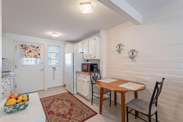 kitchen with brick wall, white appliances, beam ceiling, white cabinetry, and light tile patterned flooring