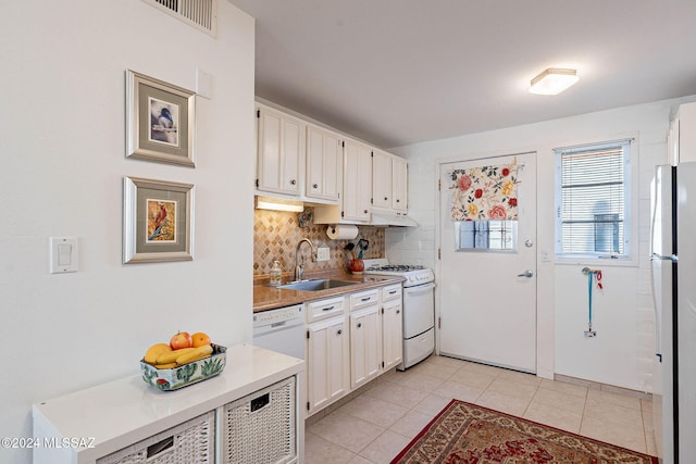 kitchen featuring backsplash, white appliances, sink, light tile patterned floors, and white cabinets