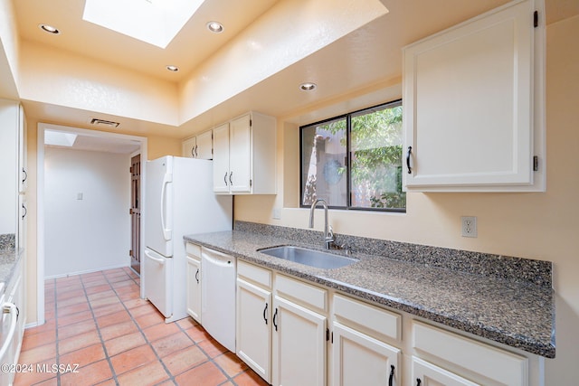 kitchen with a skylight, white appliances, sink, light tile patterned floors, and white cabinetry