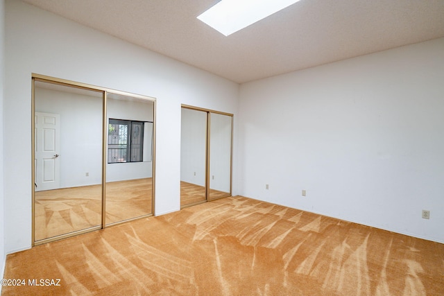 unfurnished bedroom with a skylight, carpet, and two closets