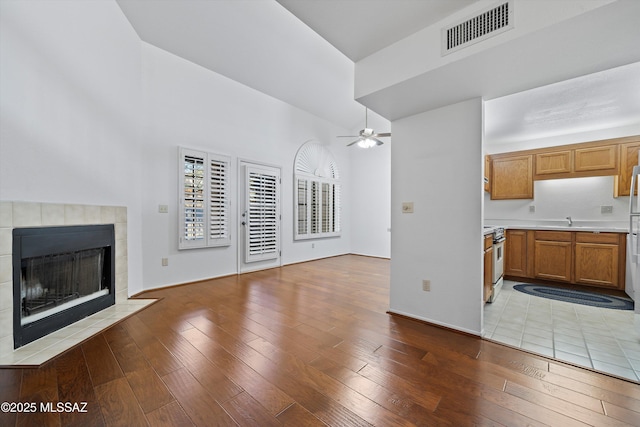 unfurnished living room with visible vents, ceiling fan, hardwood / wood-style floors, a fireplace, and a sink