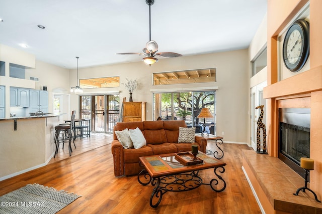 living room featuring a tile fireplace, ceiling fan, and light hardwood / wood-style floors