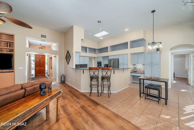 kitchen featuring kitchen peninsula, a kitchen bar, built in shelves, ceiling fan with notable chandelier, and stainless steel refrigerator