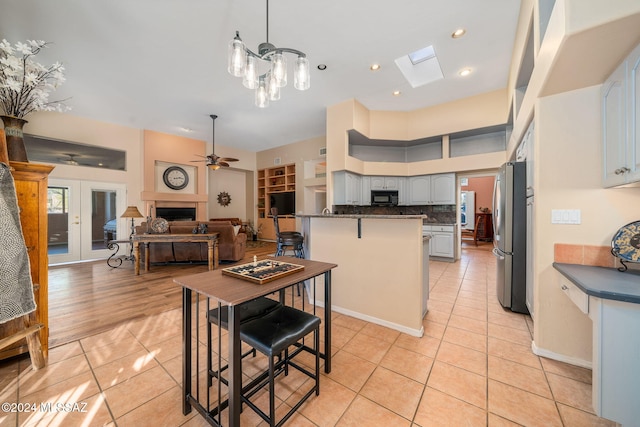 kitchen featuring gray cabinetry, ceiling fan, a skylight, stainless steel fridge, and light tile patterned floors