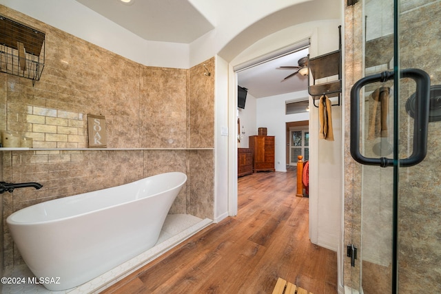 bathroom featuring hardwood / wood-style floors, tile walls, independent shower and bath, and ceiling fan