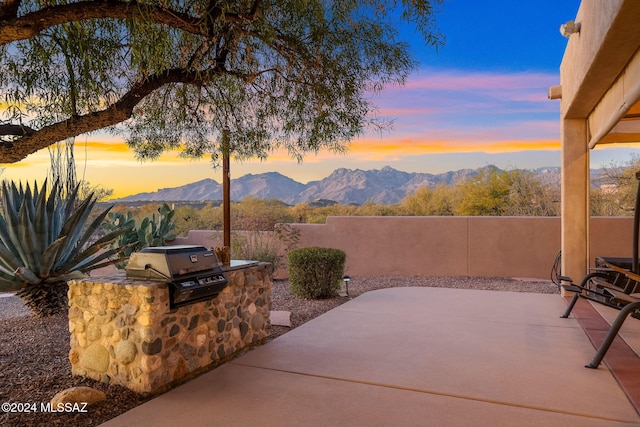 patio terrace at dusk featuring a mountain view, exterior kitchen, and grilling area