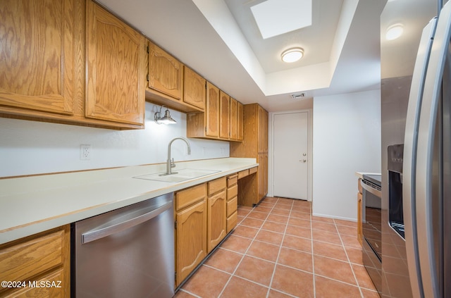 kitchen featuring a tray ceiling, sink, light tile patterned floors, and appliances with stainless steel finishes