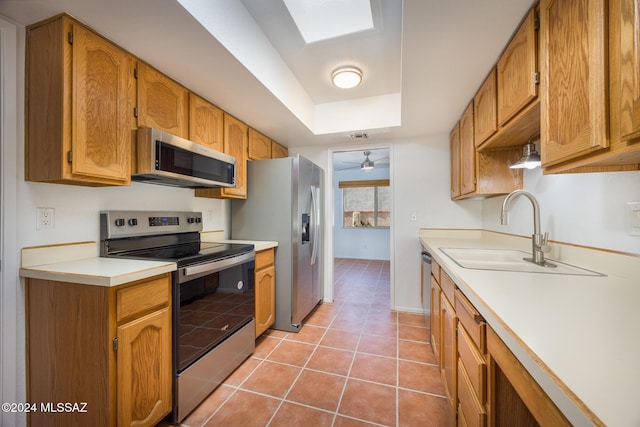 kitchen featuring appliances with stainless steel finishes, a skylight, ceiling fan, sink, and light tile patterned floors