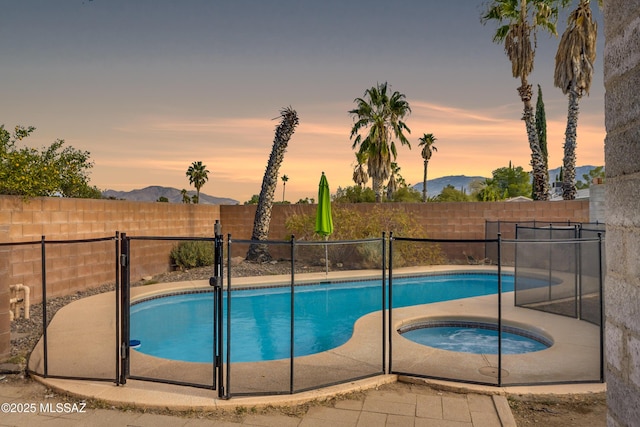 pool at dusk featuring an in ground hot tub and a mountain view