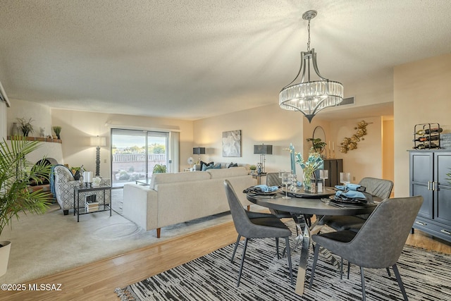 dining space featuring a textured ceiling, light hardwood / wood-style floors, and a notable chandelier