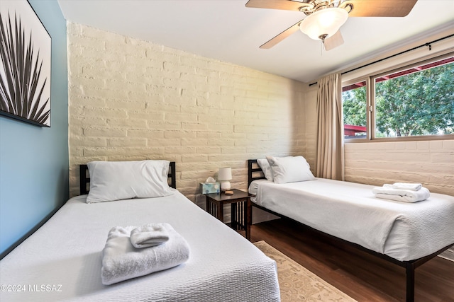 bedroom featuring dark hardwood / wood-style flooring, ceiling fan, and brick wall