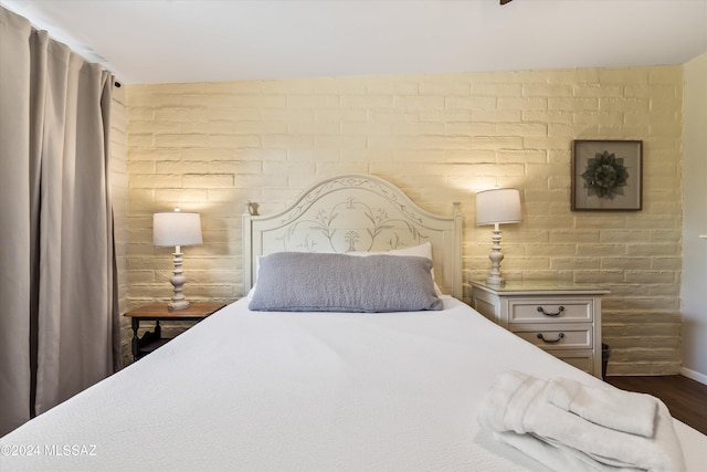 bedroom with dark wood-type flooring and brick wall