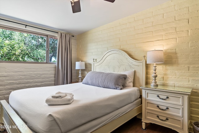 bedroom featuring ceiling fan and brick wall