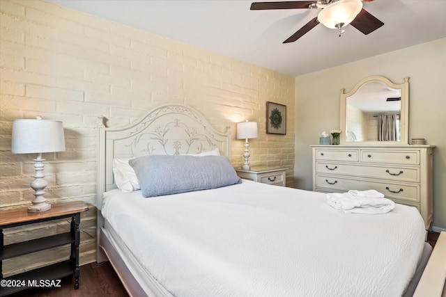 bedroom with ceiling fan, dark hardwood / wood-style flooring, and brick wall