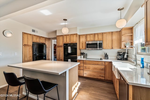 kitchen with hardwood / wood-style floors, decorative light fixtures, a kitchen island, and black appliances