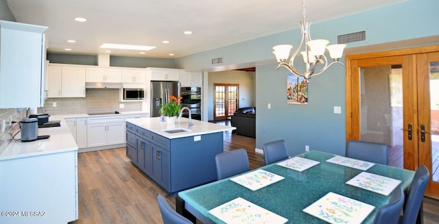 kitchen with appliances with stainless steel finishes, pendant lighting, an island with sink, white cabinets, and french doors