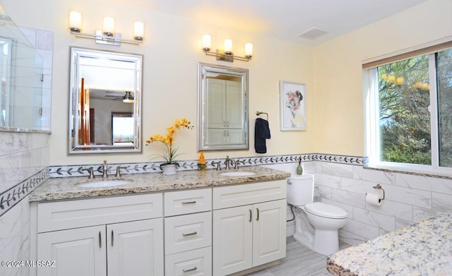 bathroom with a wealth of natural light, tile walls, vanity, and toilet