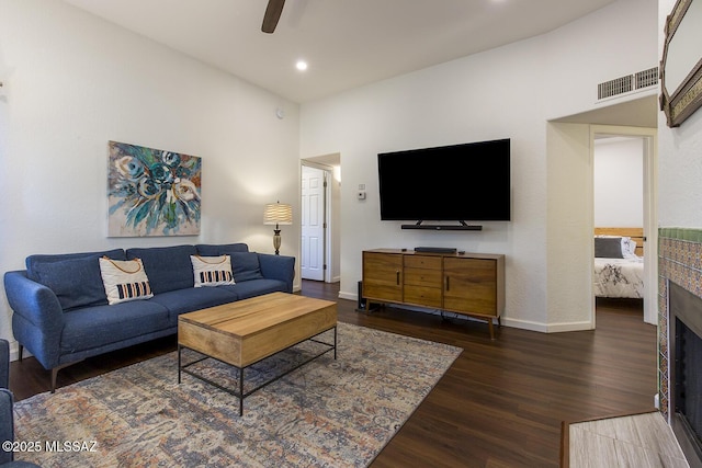 living room with a tiled fireplace, ceiling fan, and dark hardwood / wood-style floors