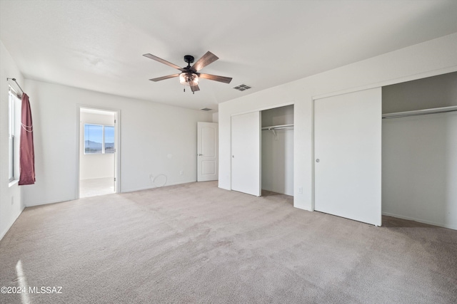 unfurnished bedroom featuring ceiling fan, light colored carpet, and two closets