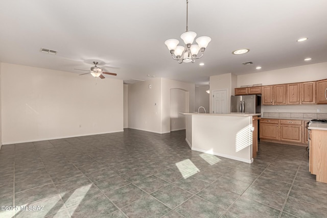 kitchen with ceiling fan with notable chandelier, pendant lighting, sink, stainless steel fridge, and a kitchen island with sink