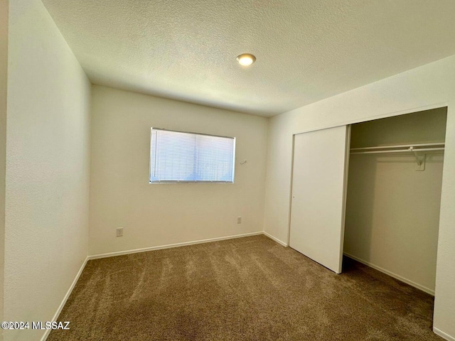 unfurnished bedroom featuring dark carpet, a textured ceiling, and a closet