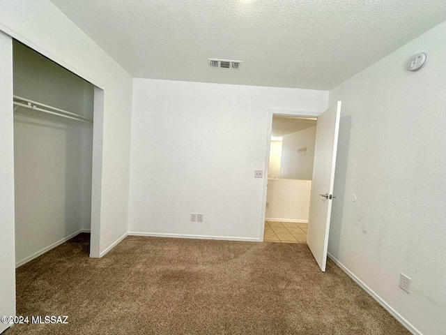 unfurnished bedroom with a closet, light colored carpet, and a textured ceiling