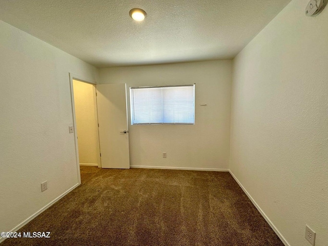 unfurnished room featuring dark carpet and a textured ceiling