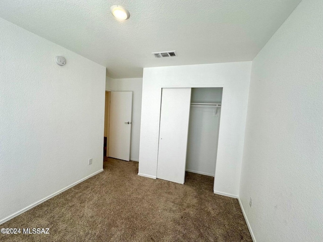 unfurnished bedroom with dark carpet, a textured ceiling, and a closet