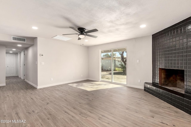 unfurnished living room featuring ceiling fan, a fireplace, hardwood / wood-style floors, and a textured ceiling