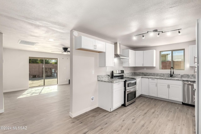 kitchen with white cabinets, wall chimney exhaust hood, light stone counters, and stainless steel appliances