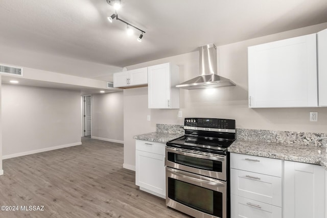 kitchen featuring white cabinets, double oven range, light stone countertops, and wall chimney range hood