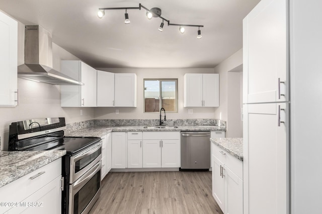 kitchen featuring white cabinetry, sink, stainless steel appliances, wall chimney range hood, and light stone counters