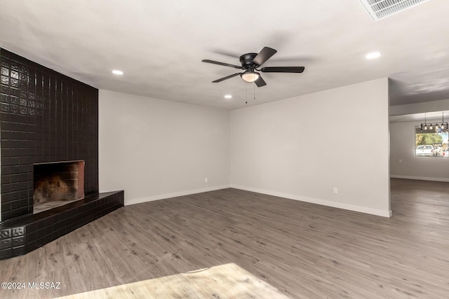 unfurnished living room featuring ceiling fan, a large fireplace, and wood-type flooring