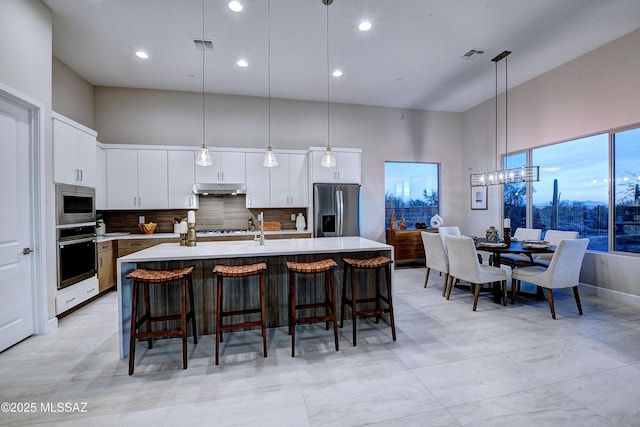 kitchen featuring decorative backsplash, a center island with sink, decorative light fixtures, and appliances with stainless steel finishes