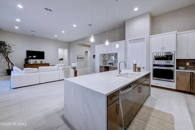 kitchen with stainless steel appliances, sink, a center island with sink, white cabinetry, and hanging light fixtures