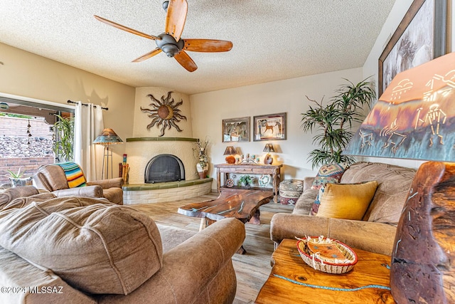 living room with ceiling fan, a textured ceiling, and a brick fireplace